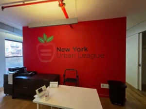 Gráfico de vinilo interior con el logo de New York Urban League en pared roja, área de recepción en Manhattan, NY
